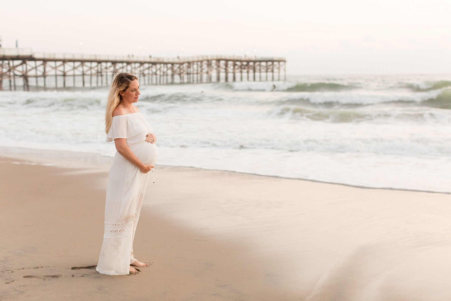 a pregnant woman holds her belly and looks at the Pacific Ocean