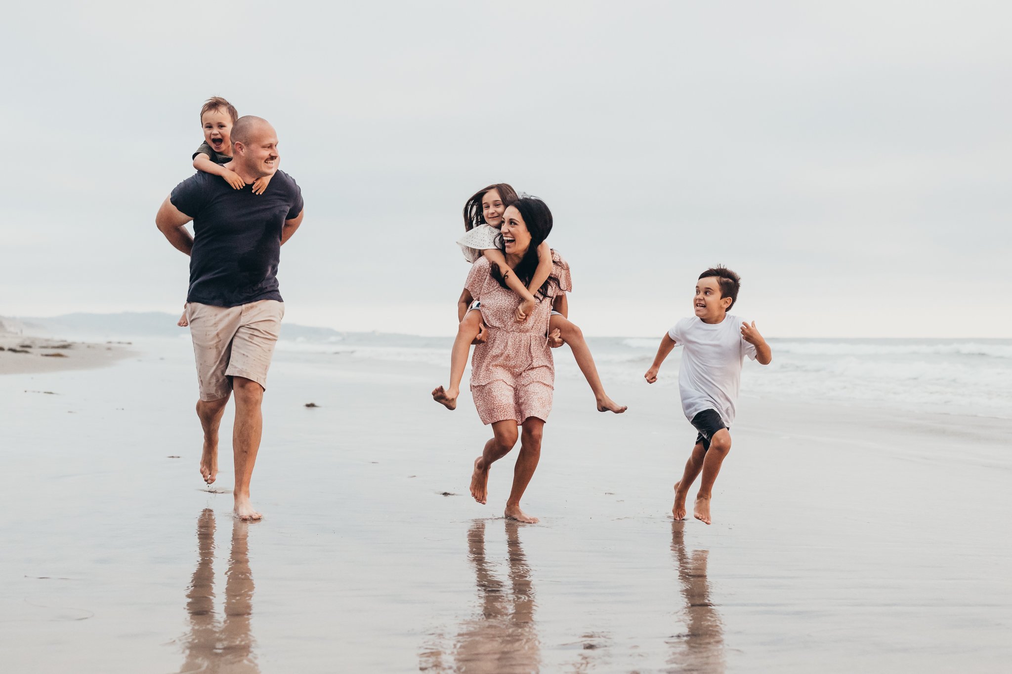 family runs around the beach in Del Mar, CA having fun together during their photography session with San Diego family photographer, Christine Dammann