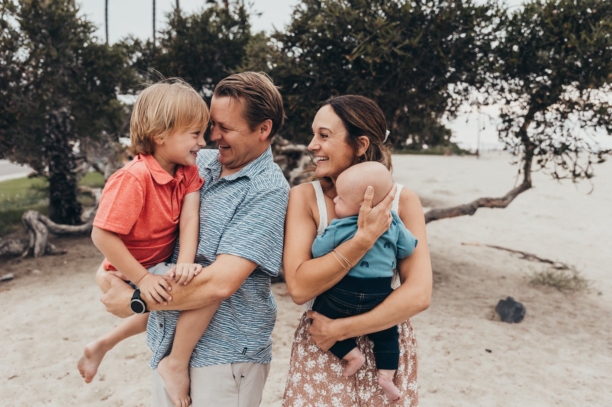 mom and dad smile and have fun with their two adorable sons on  San Diego's South Mission Beach during their family photography session with Christine Dammann