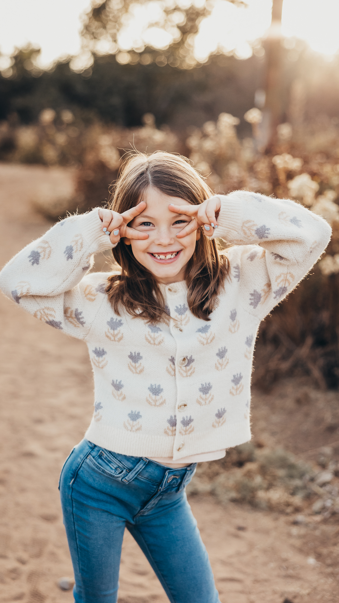 Young girl smiling and making peace signs with her fingers during a golden hour outdoor moment in San Diego. A playful family photography scene capturing the joy and energy families often experience while exploring kid friendly restaurants in San Diego.
