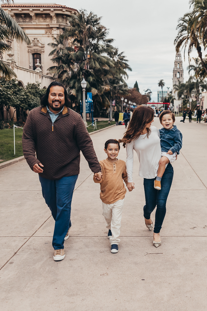 Family walking together along a palm-lined street in San Diego, smiling and enjoying a relaxed outing. A joyful moment that reflects the fun of exploring the city and visiting kid friendly restaurants in San Diego with the whole family.
