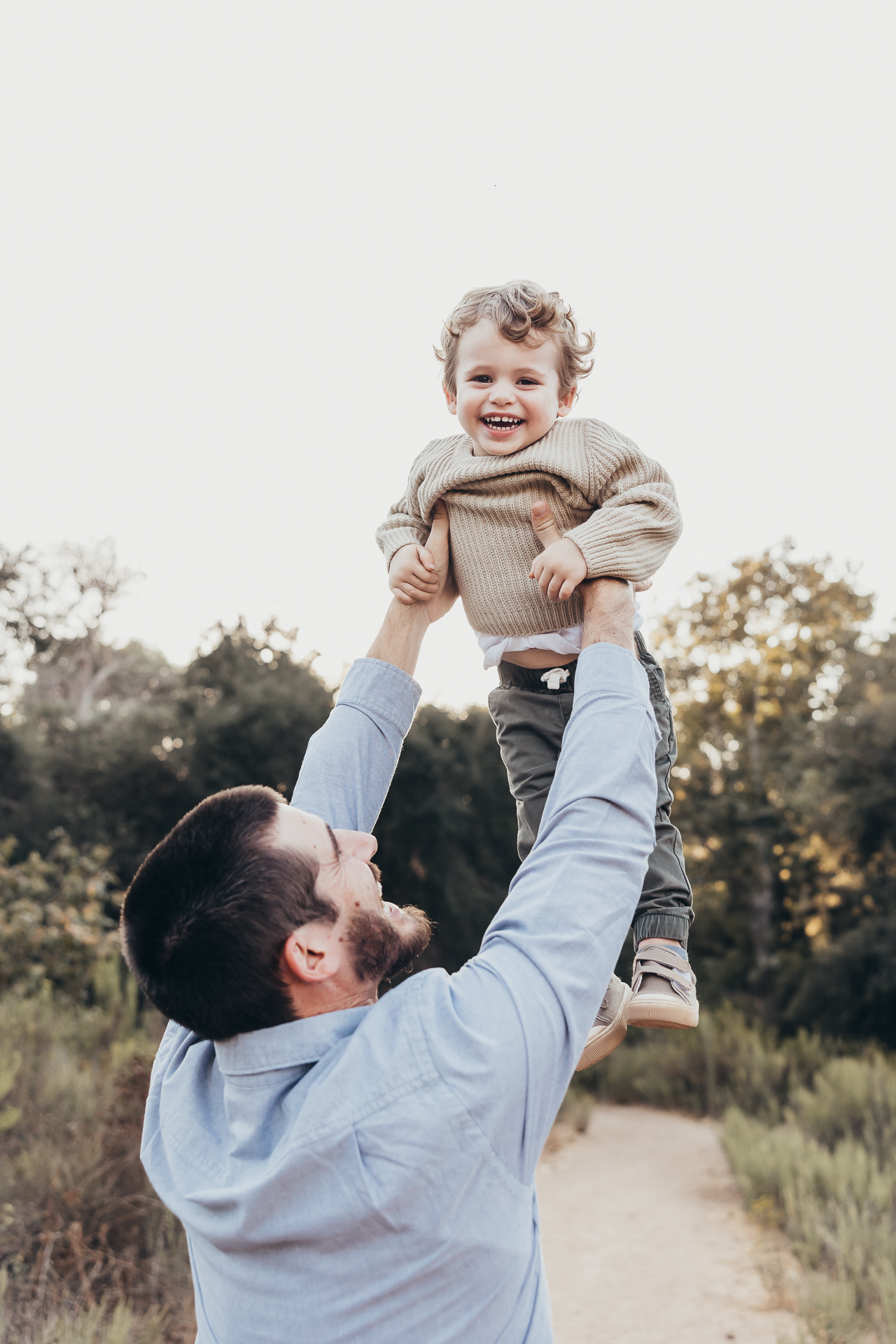 Father lifting his smiling toddler into the air during a joyful outdoor moment in San Diego. A playful family scene capturing the kind of happy memories families make before or after visiting kid friendly restaurants in San Diego together.
