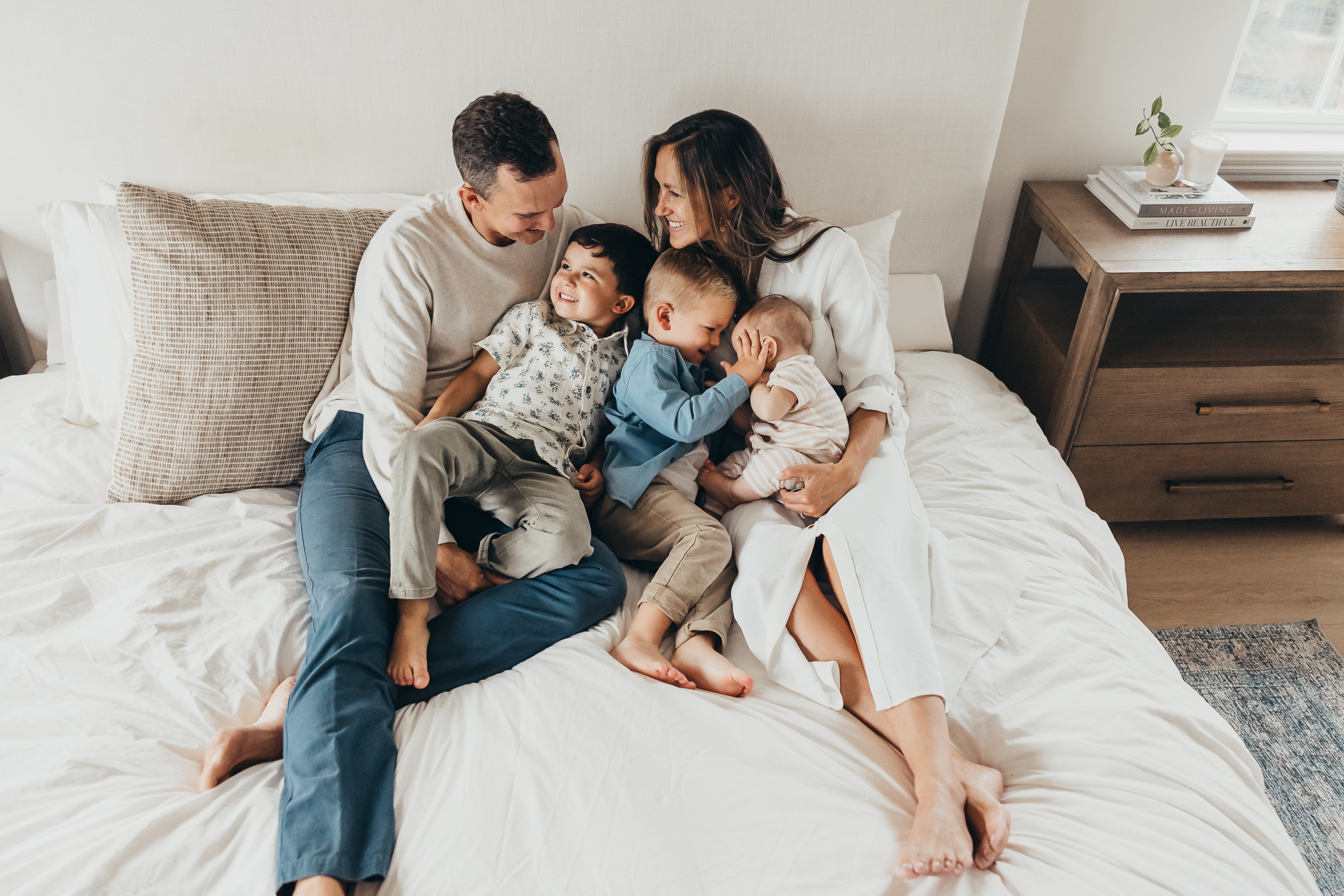 a family of five sitting on a bed smiling at eachother during their family photo session in san diego | how to get fun family photos
