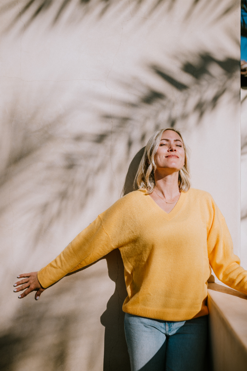 Christine Dammann stands against wall for photo with shadows of palm leaves surrounding her.