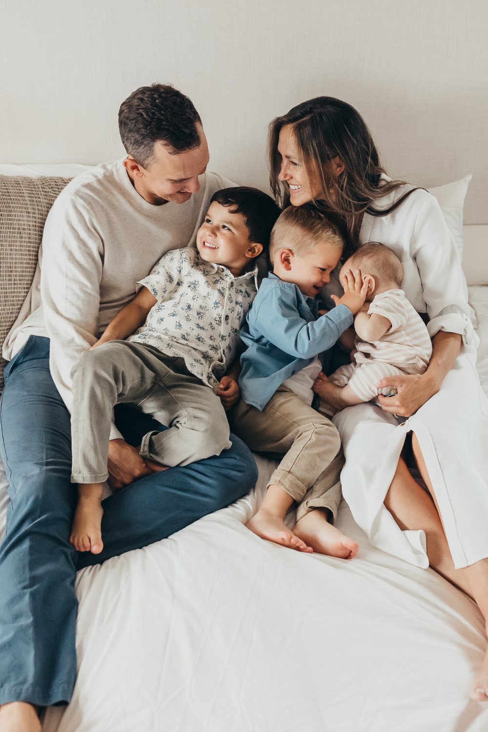 Family of five snuggling and smiling on a bed during a cozy in-home photo session.