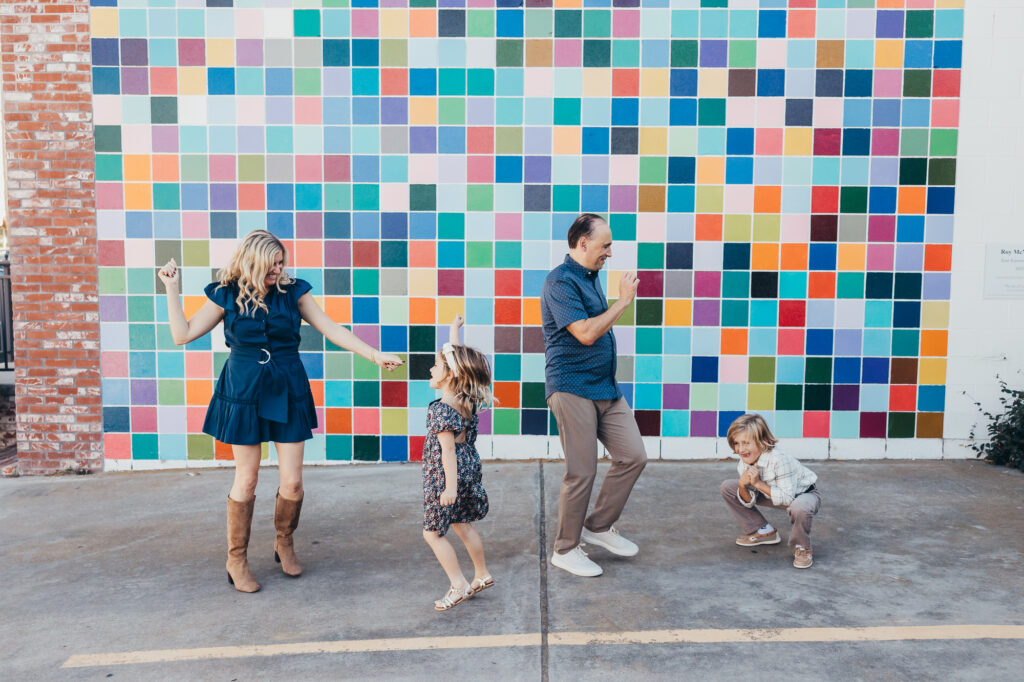 Family dancing and goofing off in front of a colorful tiled wall during lifestyle photography family session.