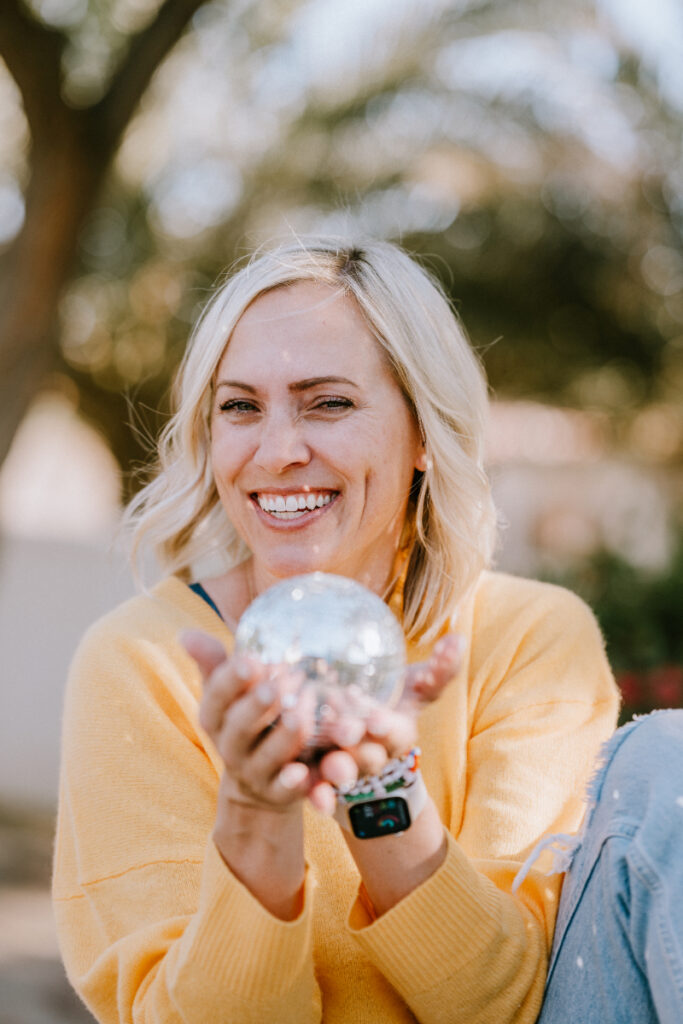 Woman smiling and holding a small disco ball outdoors, capturing the playful energy behind her approach to how to ask customers for reviews.