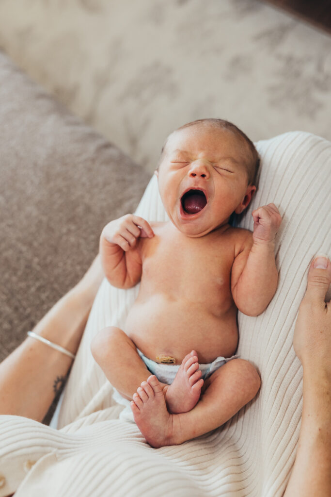 Yawning newborn cradled in parent's arms during in-home newborn photography session in San Diego.