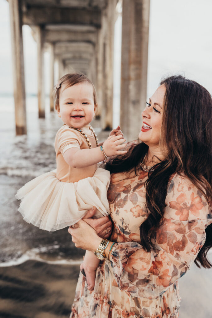 Mother holding smiling toddler near the shoreline with soft light and warm, candid connection