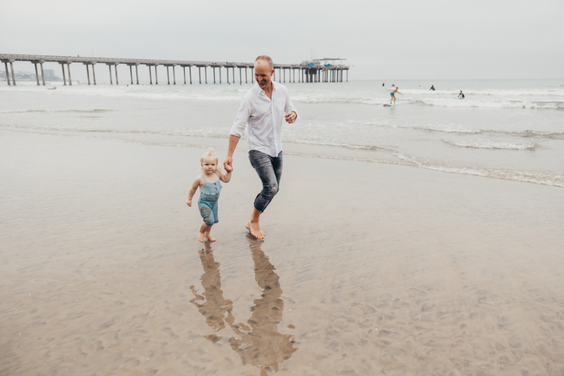 Father holding toddler’s hand near pier during a calm shoreline moment