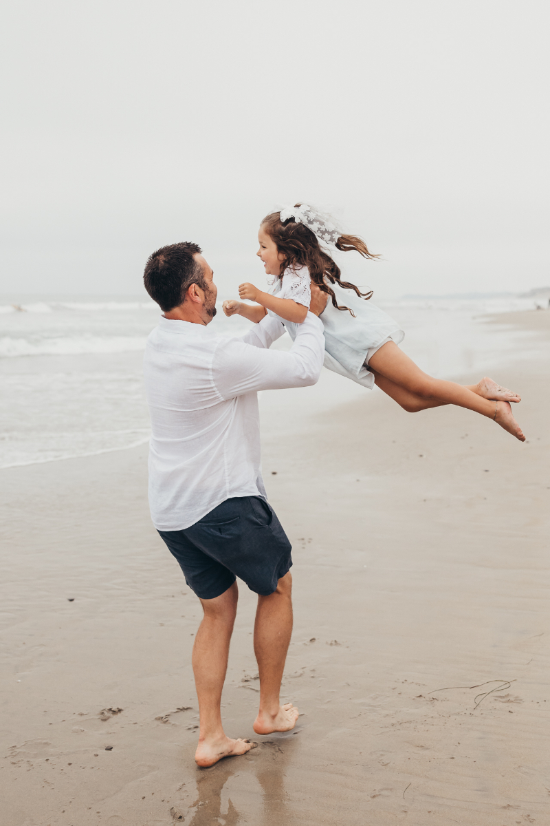 Father lifts child playfully on shoreline at one of the best beaches in San Diego during sunset