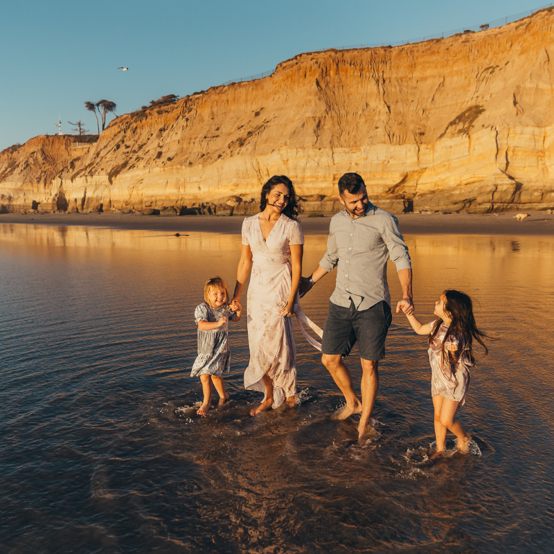 Family walking through shallow water at sunset cliffs, one of the best beaches in San Diego, warm golden light