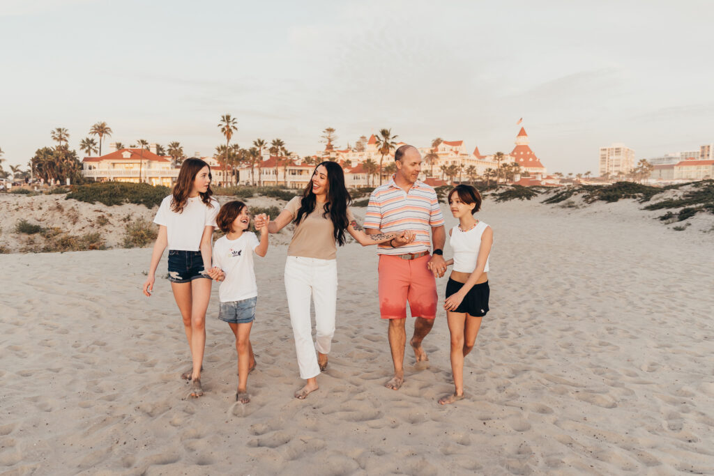 Family walking together on sandy beach with resort in background, warm sunset light candid moment
