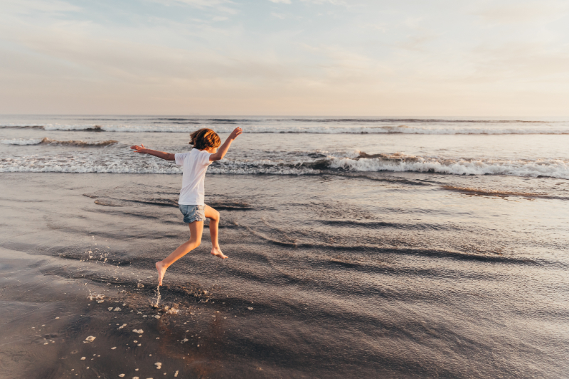 Child running through shallow waves at sunset at one of the best beaches in San Diego, candid playful moment