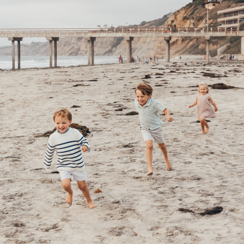 Kids running along sandy beach near pier at one of the best beaches in San Diego, joyful candid moment