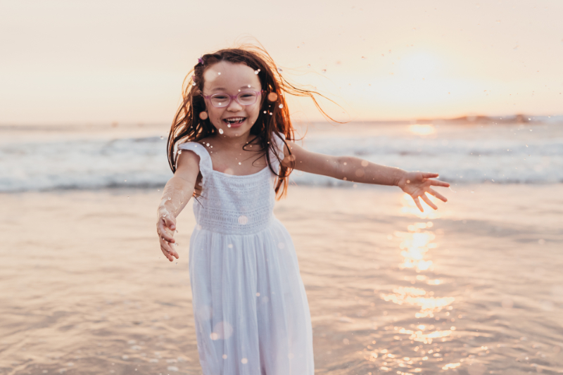 Little girl running on the beach during photography mini sessions, joyful and free in golden light