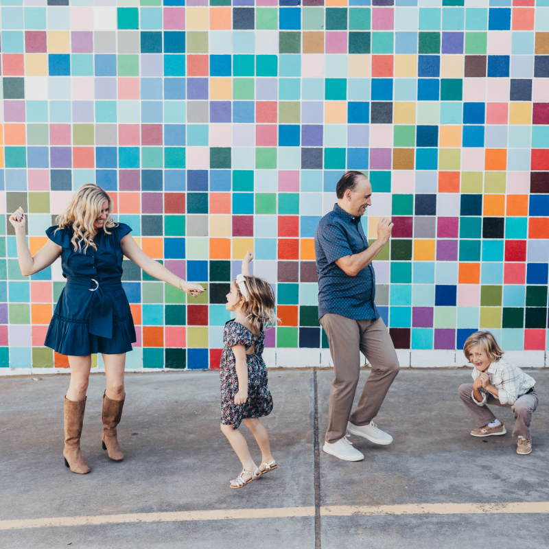 Family laughing in front of colorful wall during photography mini sessions, fun and energetic candid moment