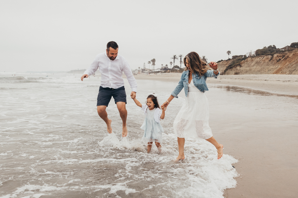 A family splashes barefoot along the shoreline during a playful beach photography session filled with movement and genuine smiles. Capturing authentic emotion and natural light is an important skill to develop when starting a photography business.
