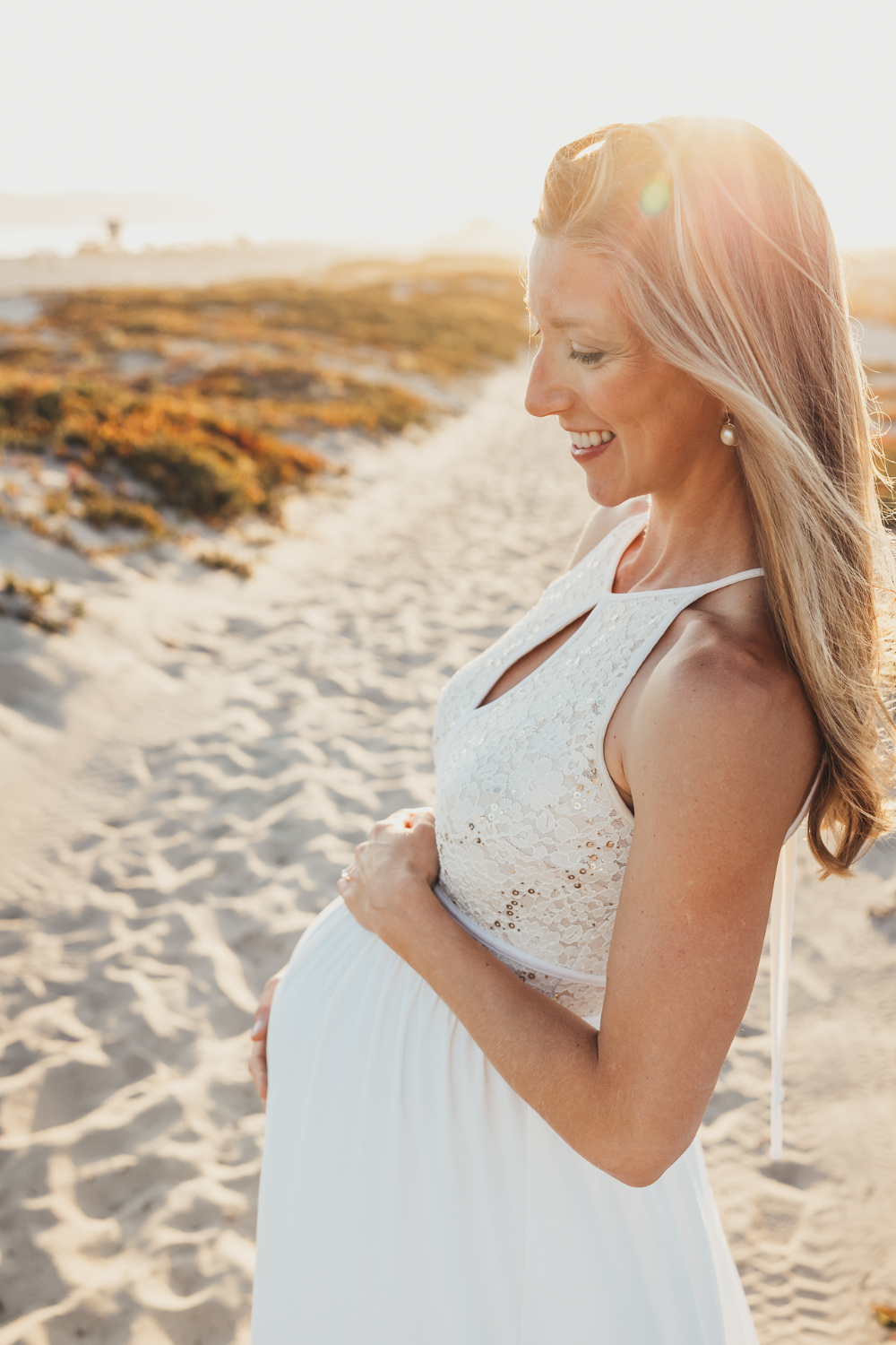 A glowing maternity portrait captured at golden hour on the beach with soft sunlight and neutral tones. Sessions like this showcase the emotional storytelling and natural lighting techniques photographers practice when learning how to start a photography business.