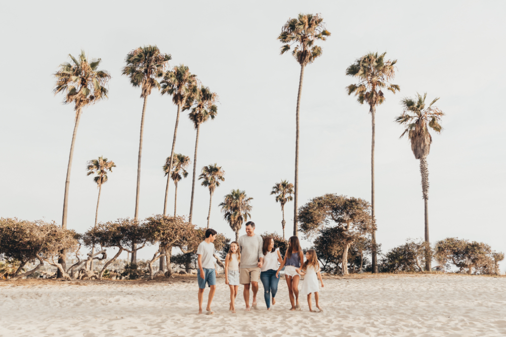 A family walks barefoot across the sand beneath towering palm trees, enjoying time together in a scenic coastal setting. This relaxed lifestyle image captures movement, connection, and the kind of authentic storytelling that helps support an effective email funnel.