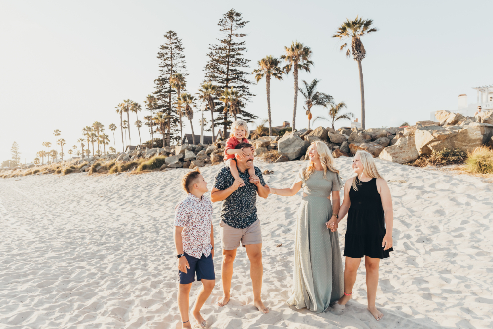 A multigenerational family strolls along a sandy beach lined with palm trees, laughing and enjoying time together. The relaxed setting and natural interactions create a timeless family portrait filled with warmth, joy, and connection.