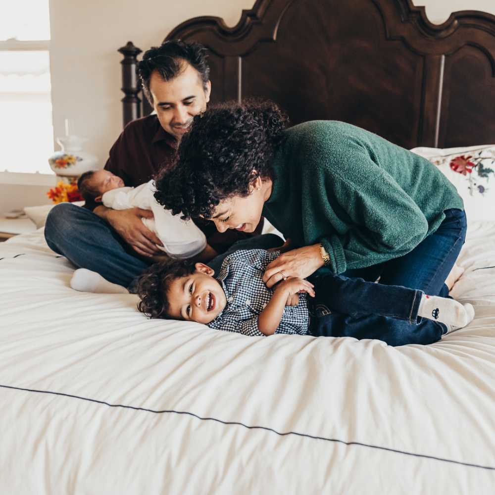 Parents spend playful time with their children on a bed at home, laughing and enjoying a candid family moment. The relaxed lifestyle setting captures genuine personalities and meaningful memories often featured when discussing photography pricing and session experiences.