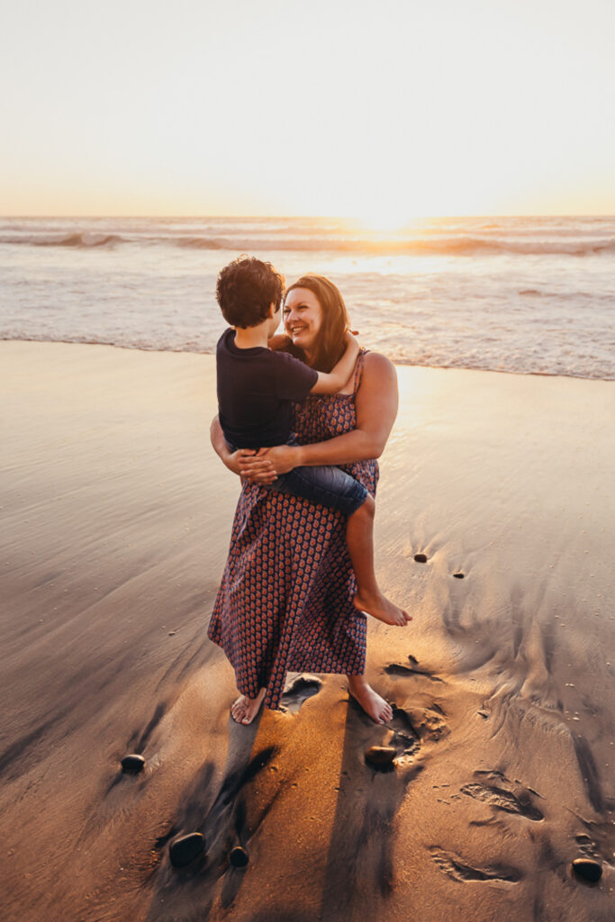 Mother holding her young son on the beach during a warm, candid family photography session at sunset.