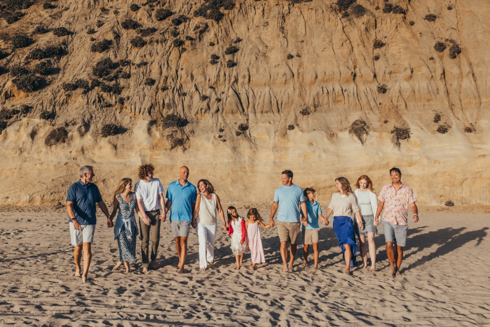 A large extended family walks together along a sandy San Diego beach in warm evening light. Extended family sessions offer another opportunity for getting more clients by continuing relationships with families as they grow and change.
