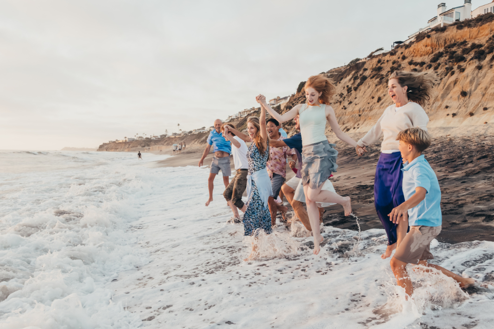 An extended family runs and splashes together at the edge of the ocean during a San Diego beach photography session. A different location, season, or activity can give returning families a new experience while documenting another stage of family life.