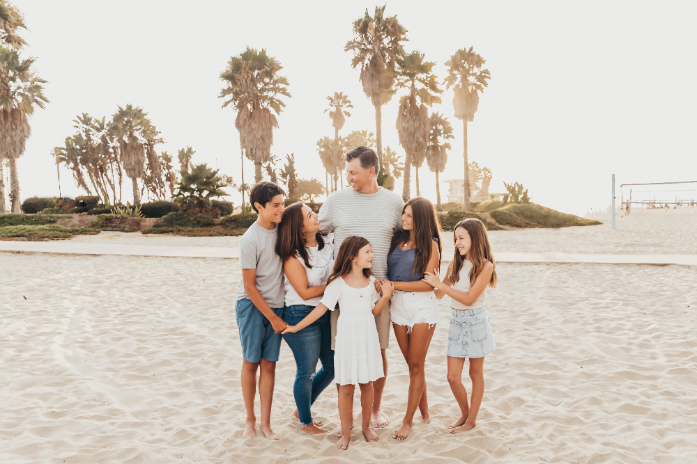 A family of six laughs together on a palm-lined San Diego beach in soft evening light. Creating a comfortable experience that families want to return to can make getting more clients feel more natural through repeat sessions and referrals.